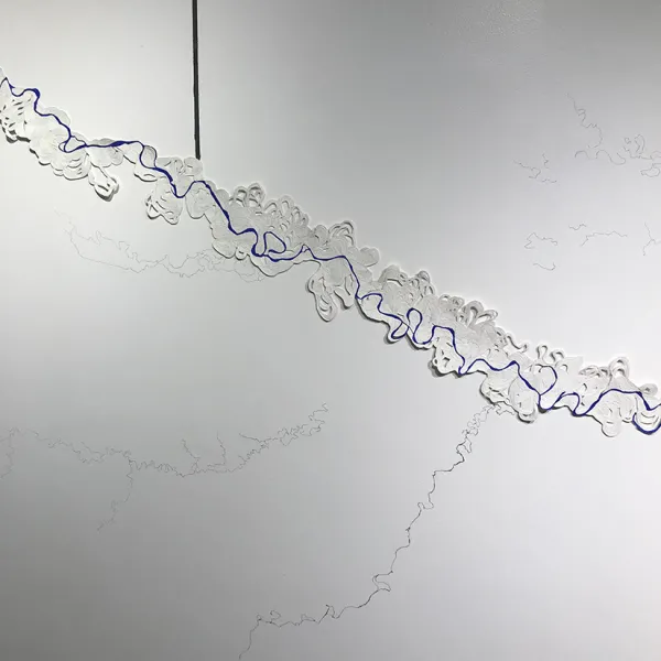 The paper is coiled so that it looks like terrain on a topographical map. There's a curved, rambling line drawn on it that looks like a river on the "map" and a straight vertical line above the image that looks like it "drew" or "traced" the line. 