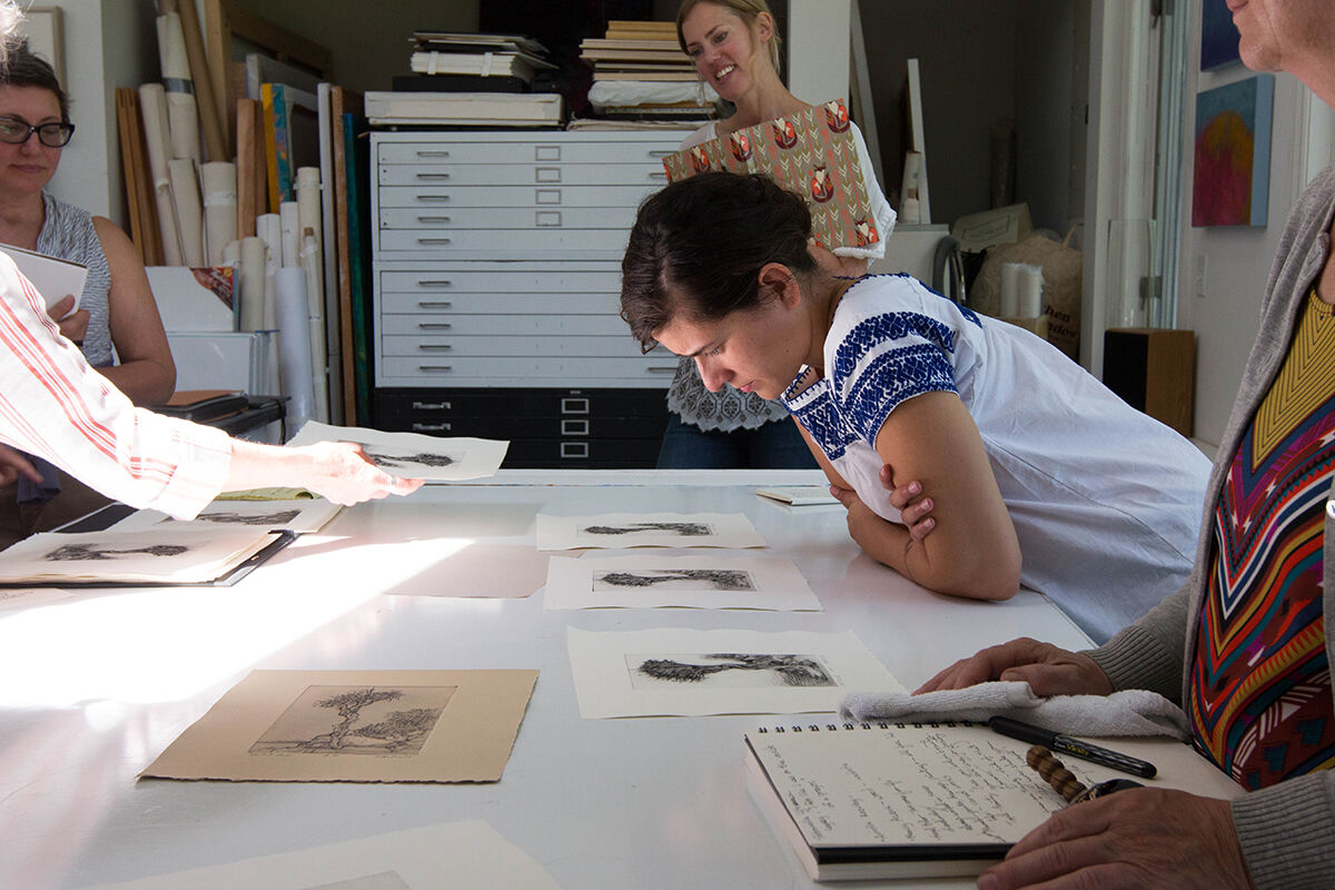 Women leaning on desk examining print artworks