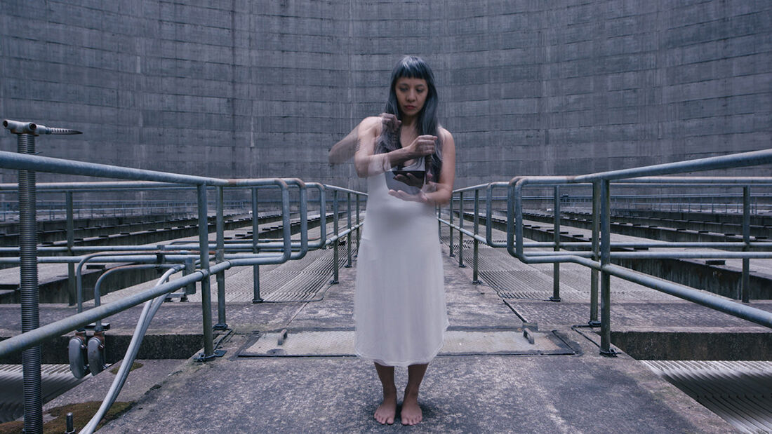 A woman in a white dress in an industrial area holding a camera-like object