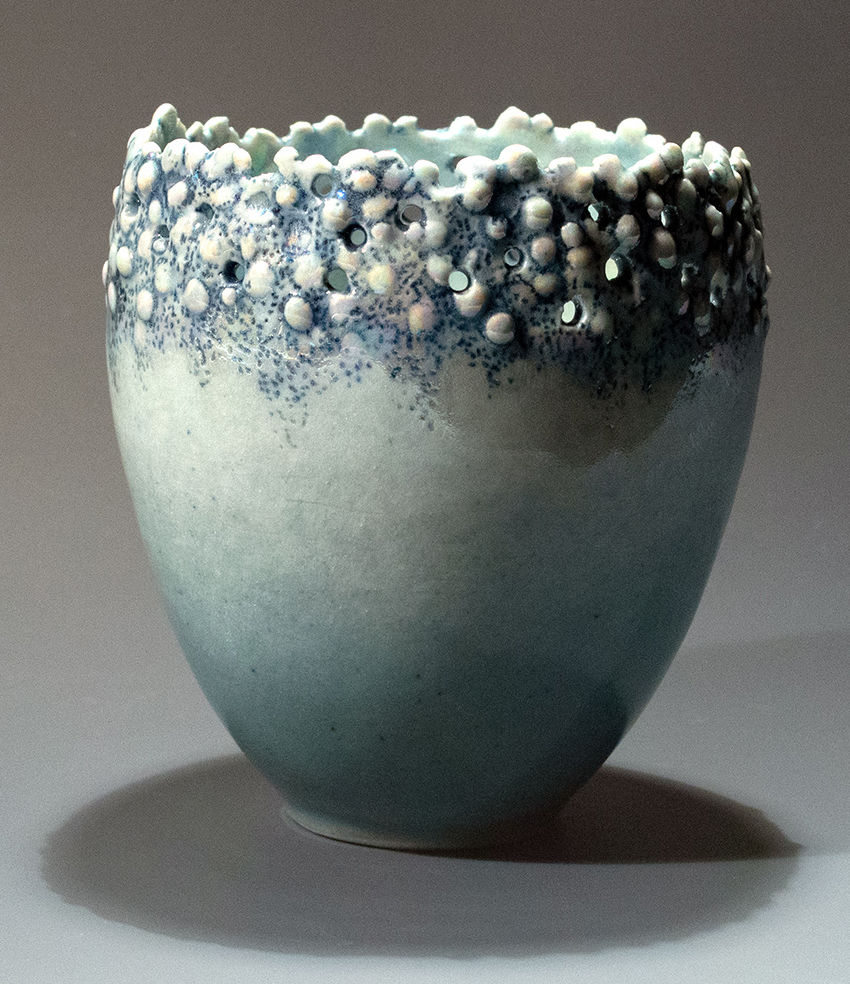Pale green cermic vessel with bubbles of glazed clay and holes surrounding the opening at the top
