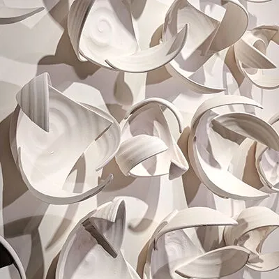 Abstract wall art in white, with shadow at left. Looks like pieces of bowls joined in ways that don't at all resemble the originals.