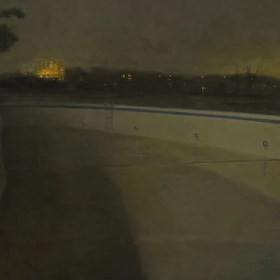 Empty outdoor swimming pool at night, with trees, cityscape, and lake in background