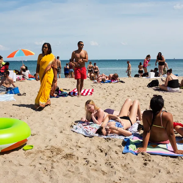Many people at the beach, all dressed in swimsuits except for one woman in a yellow sari.