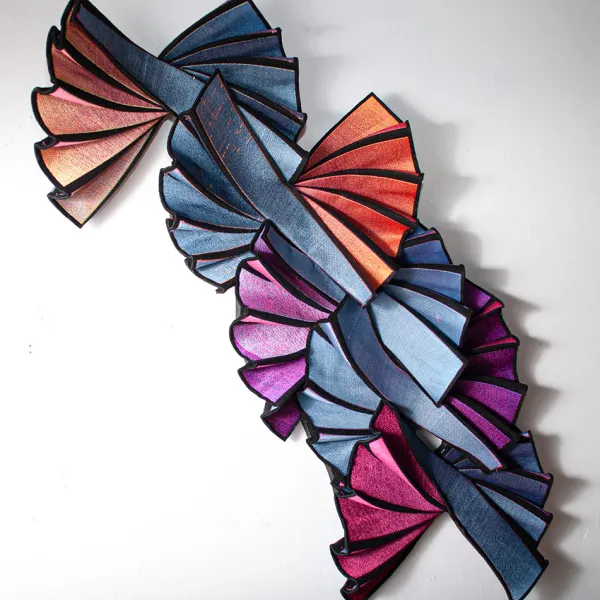 Susan Hensel, "Chromatic Flutter," digital embroidery, 42” x 31” x 5” Four folding fans made of fabric, joined together in a line. Each is metallic blue on one side and a different color on the other side. The pivot point of each fan is at its center, not at one end, so that the blue side is displayed on one side and the other color is displayed on the opposite side.