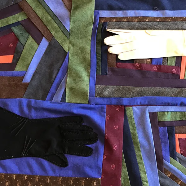 Rita Collins, "Covid Quilt #1 (Segment A)," fabric, gloves, thread, entire quilt: 39” x 44” Quilt segment consists of four panels. The top right panel has a white glove reaching toward the center. The bottom left panel ahs a black glove reaching toward the center. The other panels have layers of bands of different colors laid out in the shape of a pentagon.