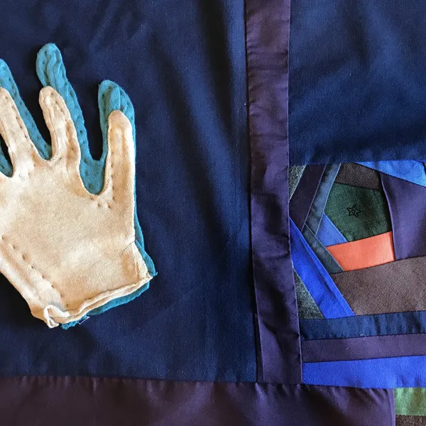 Quilt panel with a white glove on top of a blue glove. Both have stitching around the edges but are open at the wrist.