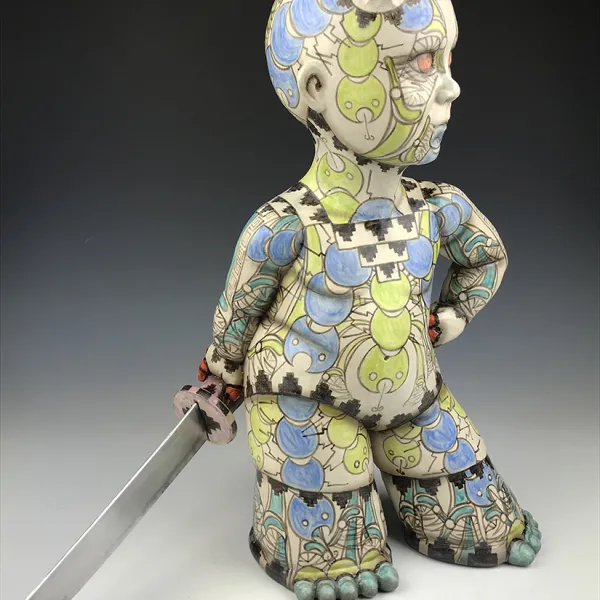 A ceramic human-like figure, tattooed from head to foot, with small horns on its head. Its legs and feet are wide. It's carrying a sword.