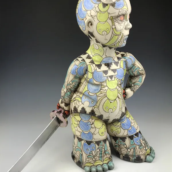 Guillermo Guardia, Ocllo Nikkei, 2019, ceramics, underglazes, clear glaze, aluminum blade, 24 x 10” A ceramic human-like figure, tattooed from head to foot, with small horns on its head. Its legs and feet are wide. It's carrying a sword.