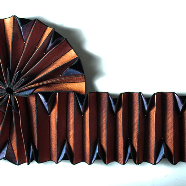 Copper-colored accordion-pleated fabric curled in a circle and then stretched out to the right in a straight line.