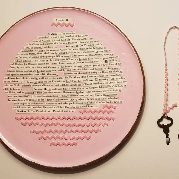 Brenda Olson - "He Shall," mixed media, 8" x 12" A pink plate with strips of paper glued on it that contain (parts of) Article II, Sections 1-4 of the United States Constitution. There's also some pink bric-a-brac on the plate. To the right of the plate is pink bric-a-brac with an old-fashioned key on each end.