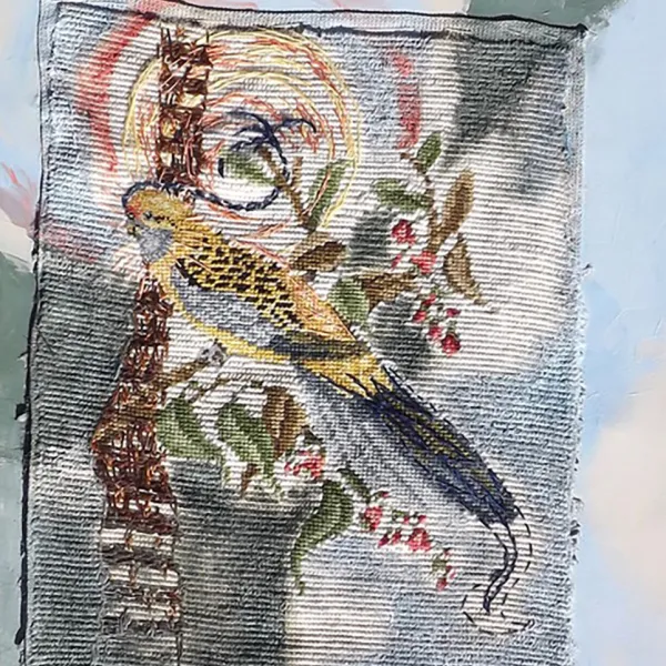 A bird and flowers are stitched on a crewelwork canvas which is on top of a painting of sky and leaves and the sun the painting is a background for the stitching.