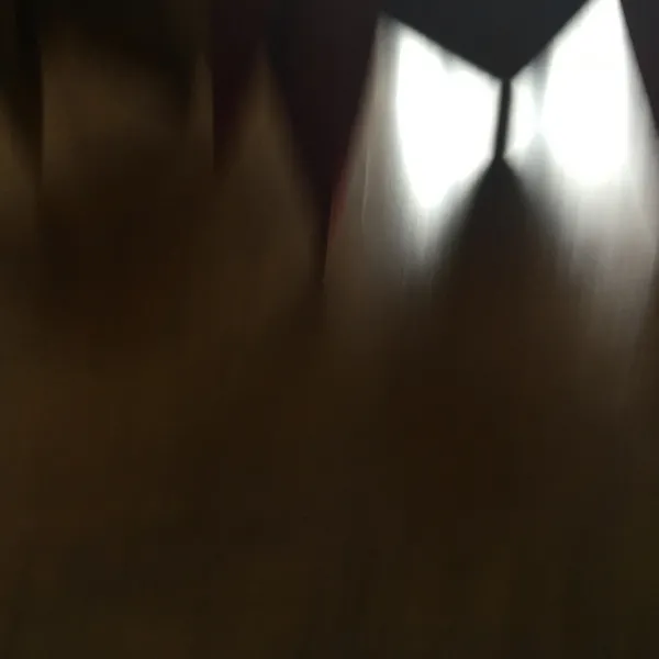 Abstract, background is brown and dark gray with traces of other colors and dark shapes pointing downward. There's an M-shaped part where the light is getting through.