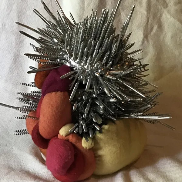 Sculpture with round fabric objects like fruit or gourds and a large "flower" on top make of screws pointing outward.