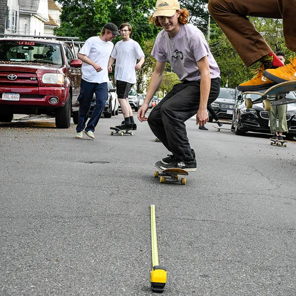 Sarah Kilgallon, "Taking Air, June 6, 2020," digital photograph, 5” x 7” Teenagers skateboarding in a parking lot. A tape measure on the ground measures the distance between the photographer and the closest skater.