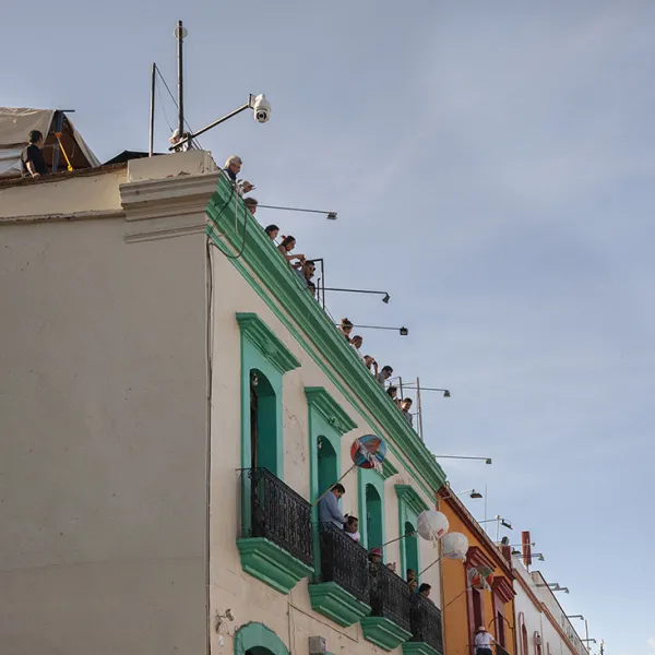 × Emelin Ventura Gonzalez - "Andador Turistico 1," photography, 13" x 19" Colorful buildings with people standing on balconies and also on the roof. Andador Turistico is a tourst attraciton in Oaxaca, Mexico.