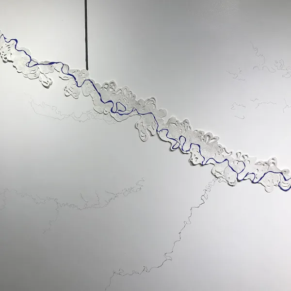 Rina Yoon, Trace of Time, 2019 (detail), hand-coiled paper, pigment, graphite, approximately 8 feet tall x 16 feet long The paper is coiled so that it looks like terrain on a topographical map. There's a curved, rambling line drawn on it that looks like a river on the "map" and a straight vertical line above the image that looks like it "drew" or "traced" the line.