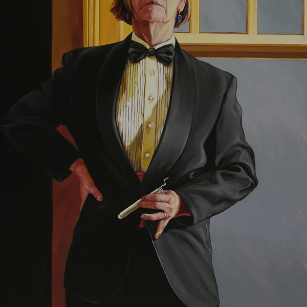 Woman in tuxedo and bowtie, holding a cigar, standing by a window.