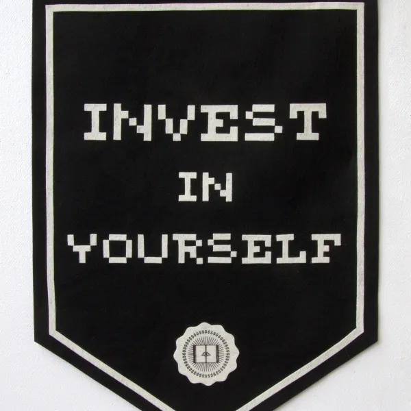 Experientia Docet, 2023, polyester felt, serigraph, 34"x24" Black flag with the text "Invest in yourself" written on it and a logo below