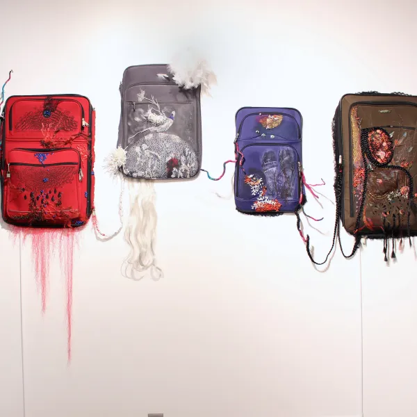 Liminal Spaces, 2026; Suitcase flaps, synthetic hair, beads, fabric, ink, and two videos on DVD players (color, 2 minutes);  90 x 96 x 4 inches