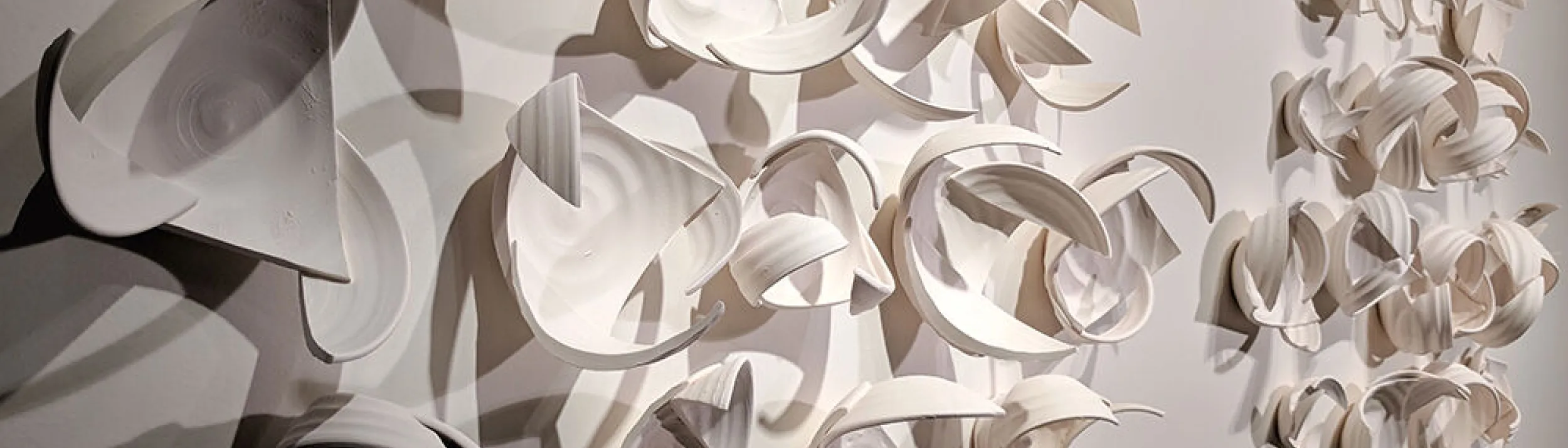 Abstract wall art in white, with shadow at left. Looks like pieces of bowls joined in ways that don't at all resemble the originals.