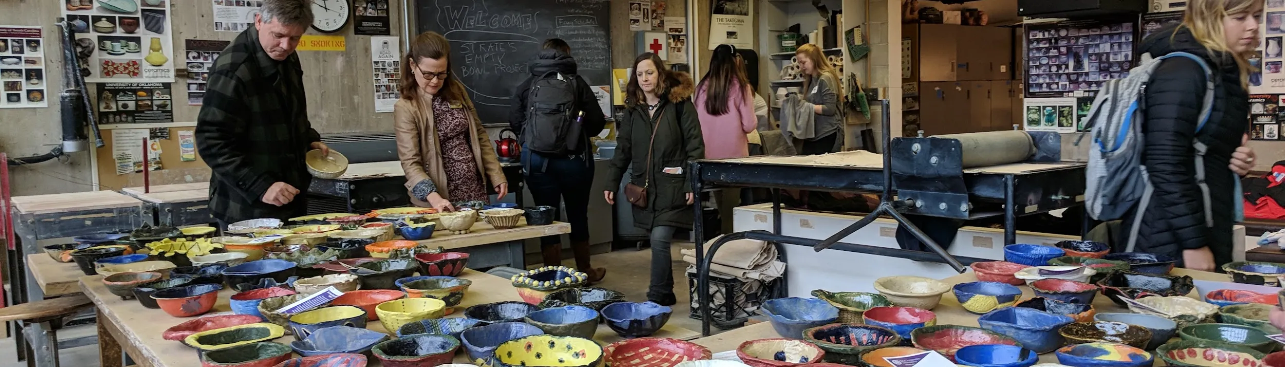 Colorful bowls laid out on tables, with people looking at them.