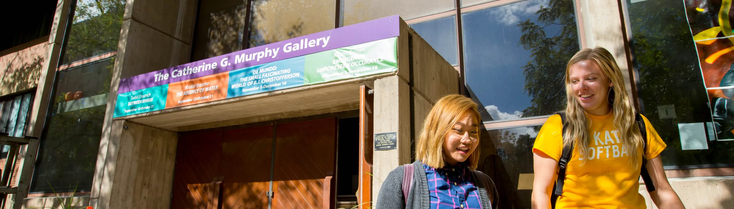 Gallery building in backgorund as pair of students talking to one another stroll away from it.