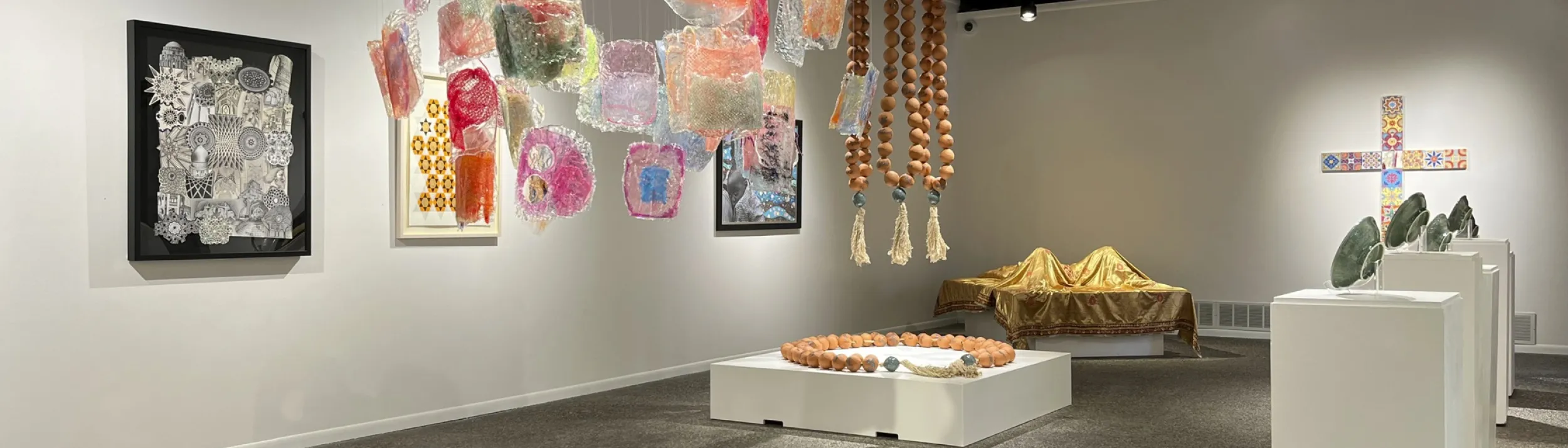 A colorful gallery exhibit full of hanging glasswork and pottery on stands.