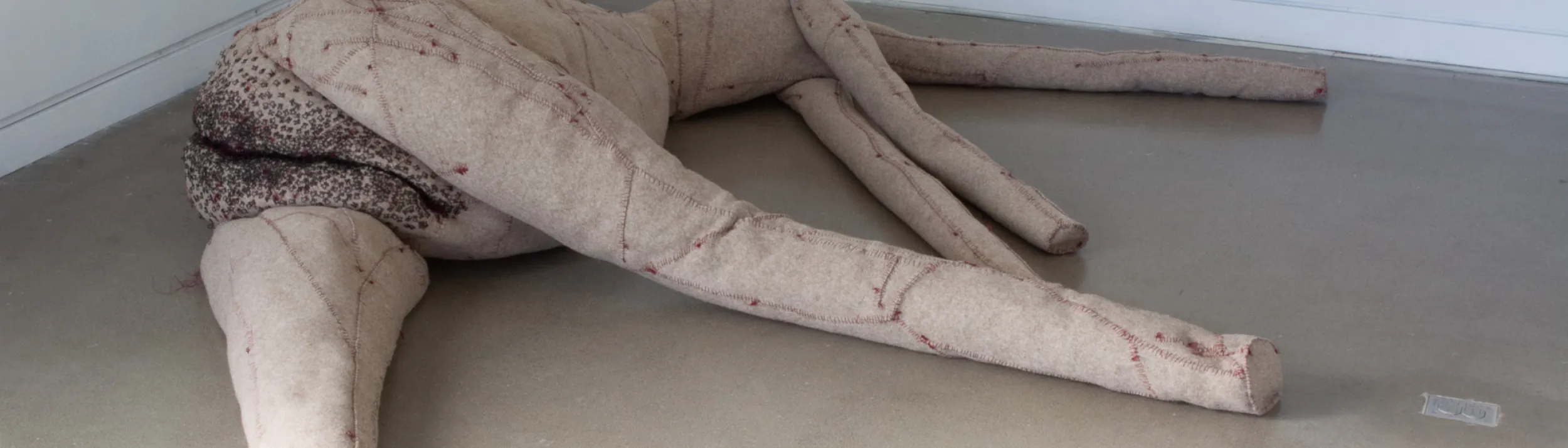 An oversize sculture of a body, mixed media including wool felt, fiber fill, sewing patterns, cotton thread, sewing hardware;
