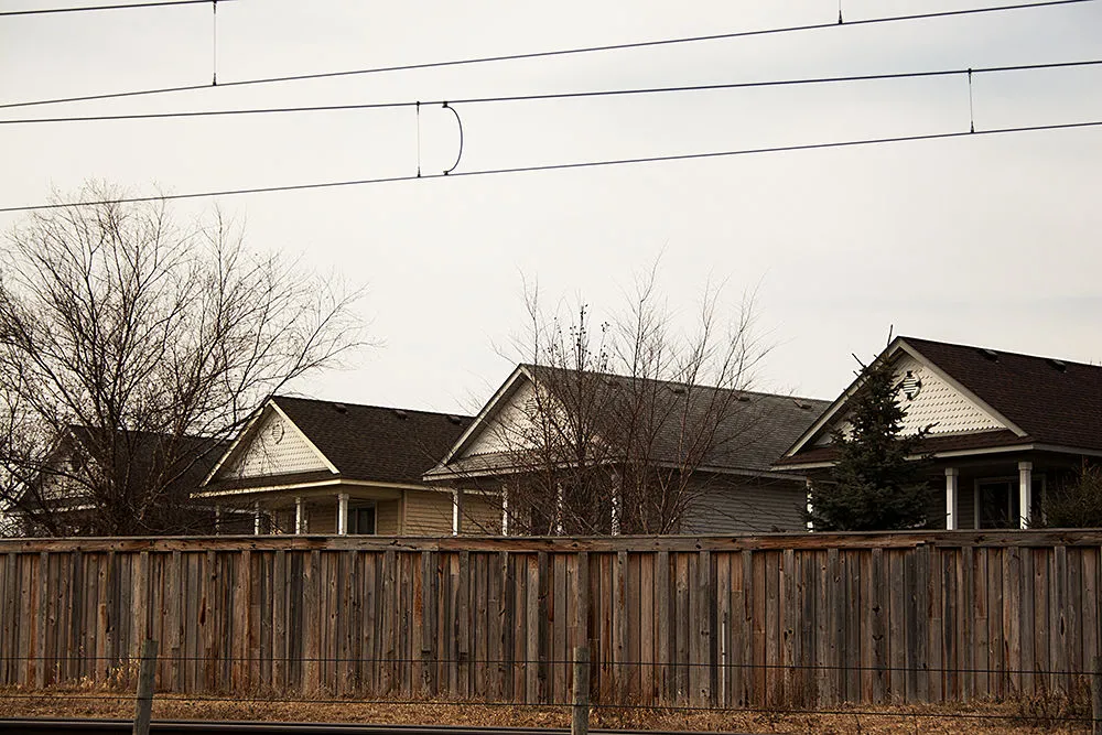 Photo of 4 house rooflines behind a brown wooden fence, power lines overhead