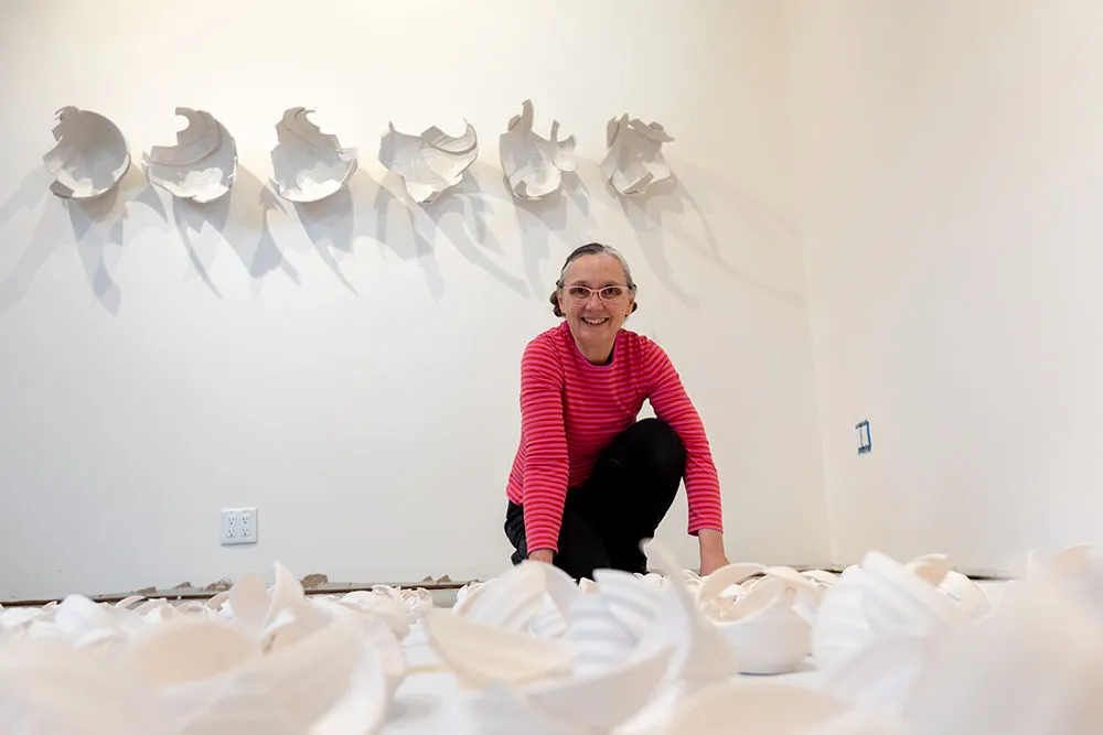 Monica Rudquist in her studio, with six abstract sculptures on the wall and many pieces on the floor which will be used to construct more of the abstract wall sculptures.
